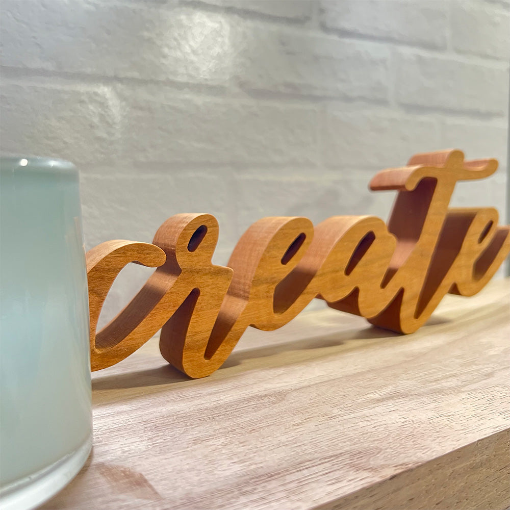 A wooden sign with the standing word - CREATE sitting on top of a shelf.