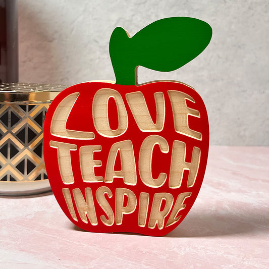 A red standing apple with the words Teach Love Inspire on it.