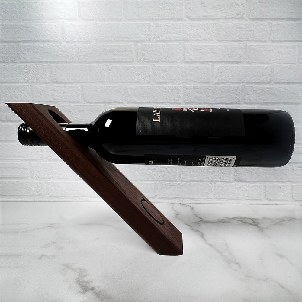A wooden balancing wine bottle holder with a bottle in it.