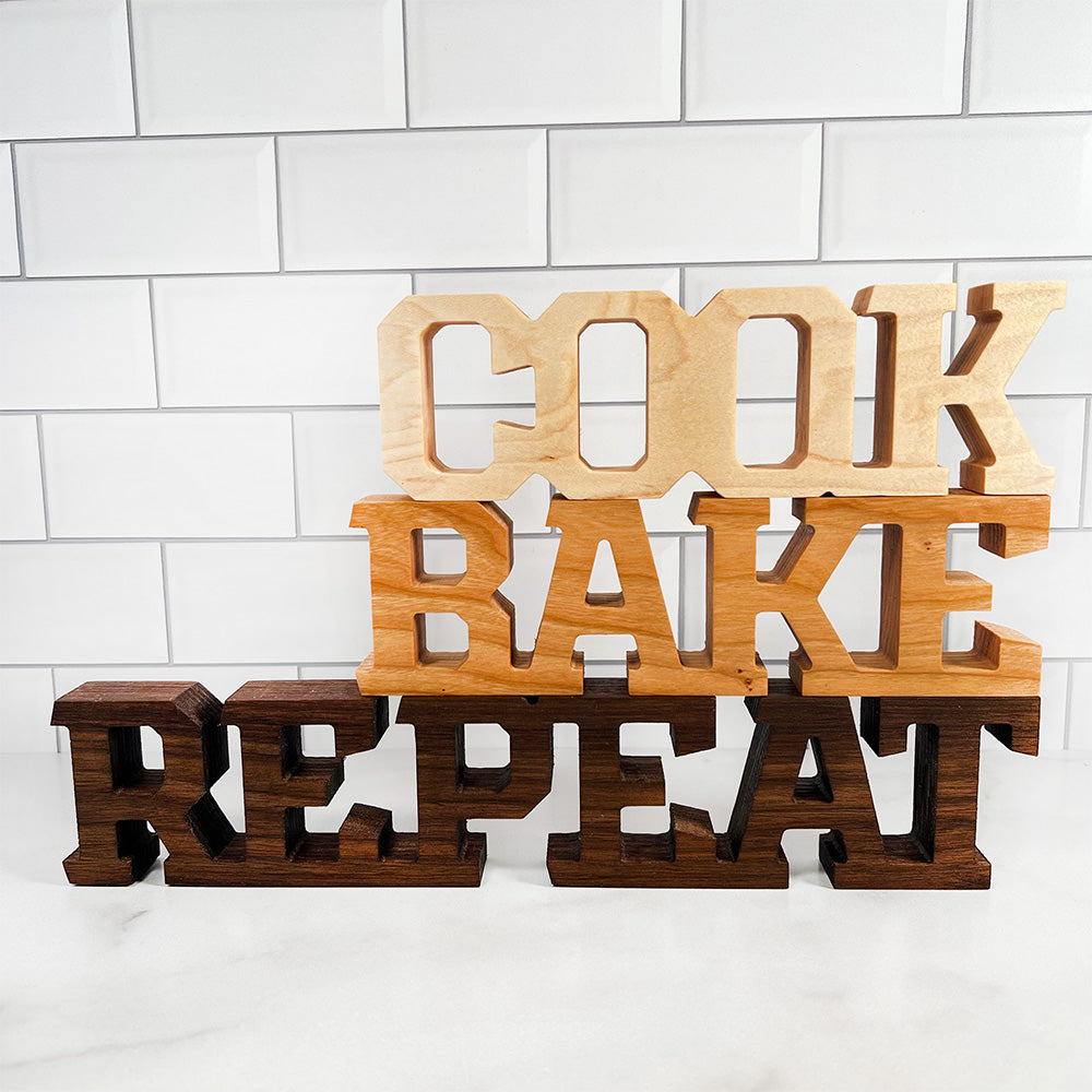 A wooden sign that says Standing words - Cook Bake Repeat.