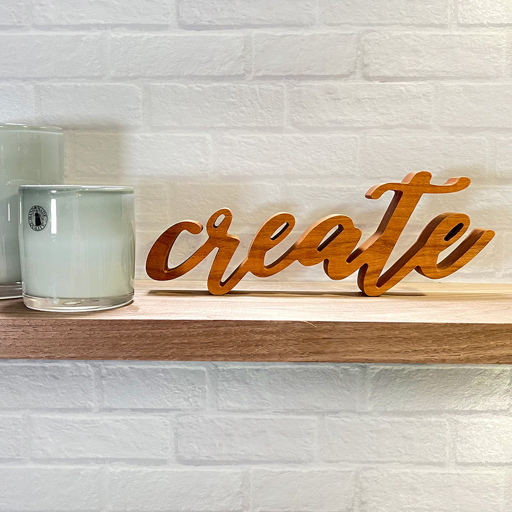 A wooden sign with the standing word - CREATE sitting on top of a shelf.