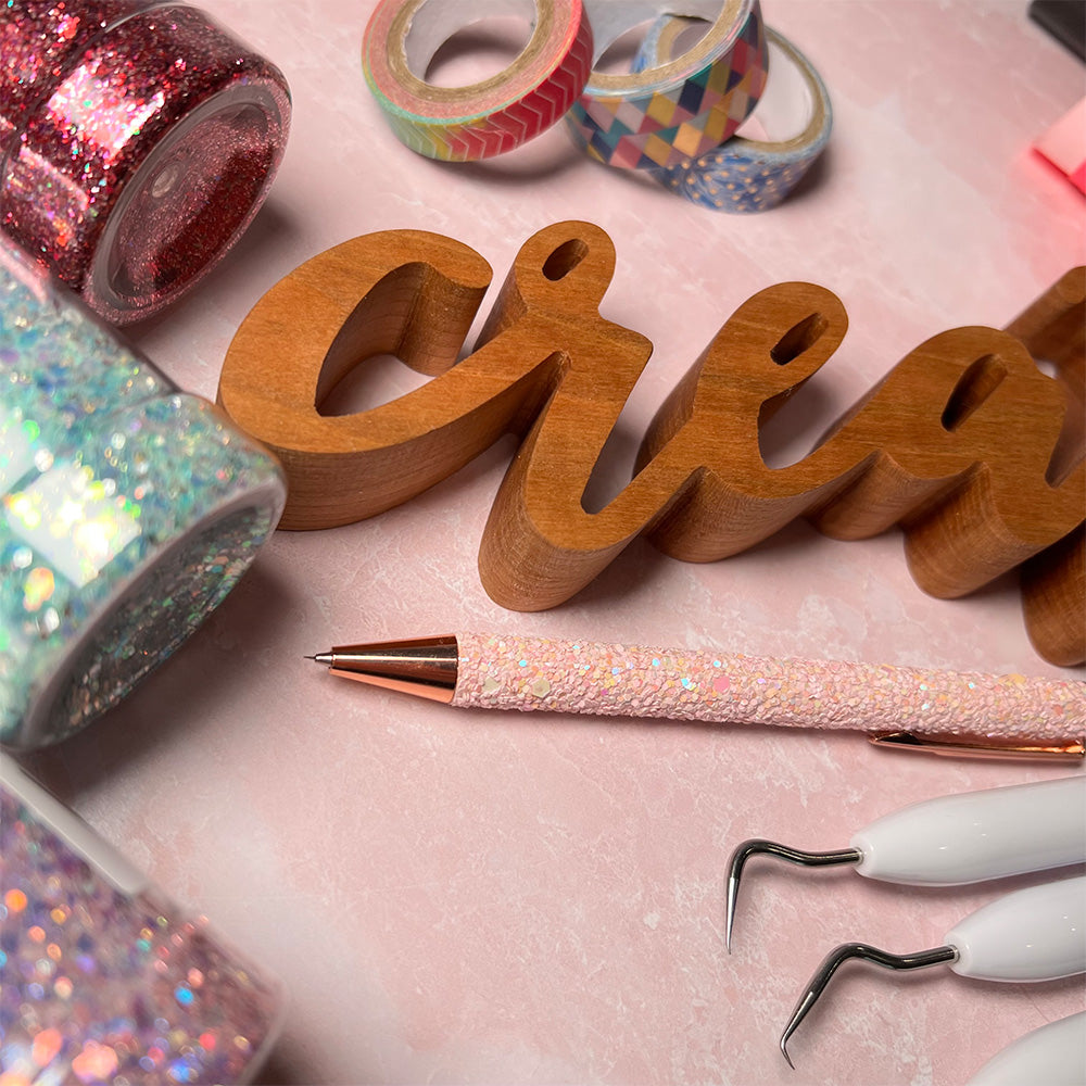 A variety of craft tools and supplies are arranged on a pink background, including the standing word - CREATE.