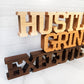 A wooden sign that says Standing words - Hustle Grind Execute.