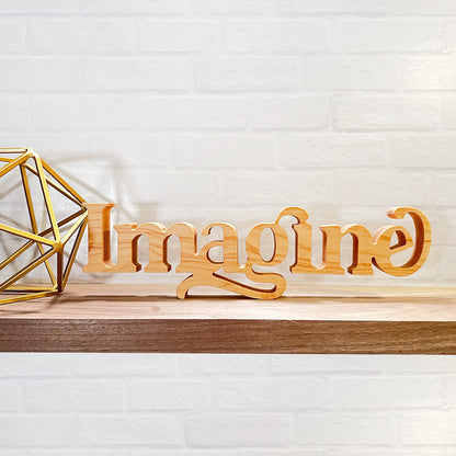 A wooden sign with the standing word - IMAGINE sitting on a shelf.