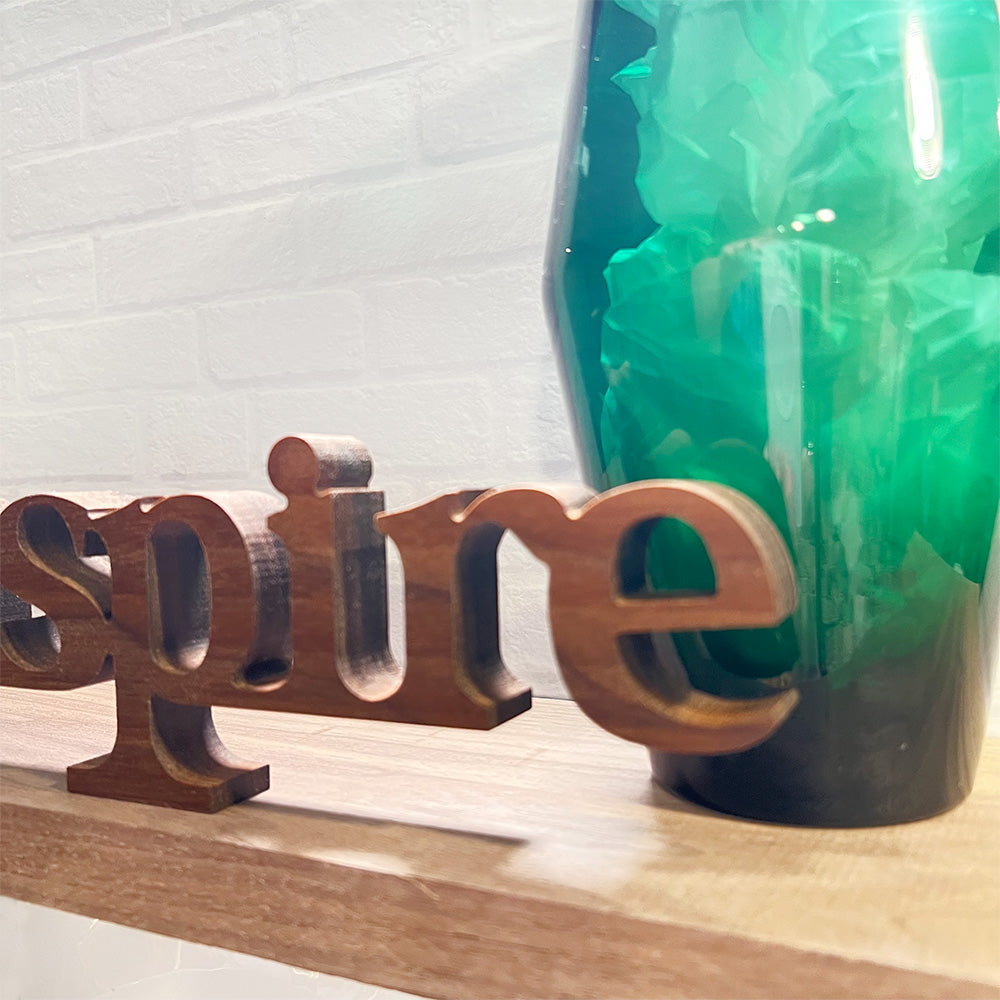 The standing word - INSPIRE is on a shelf next to a green vase.