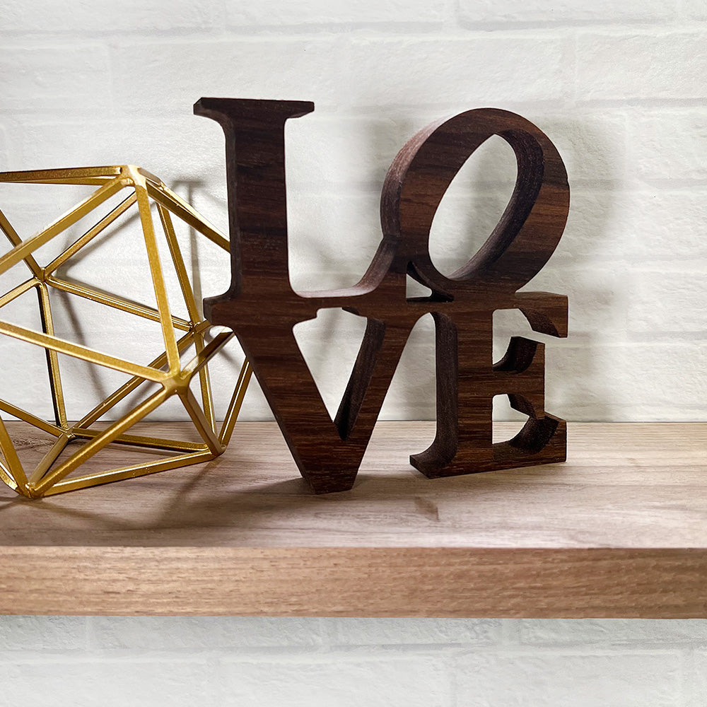 A wooden sign with the Standing word - LOVE on top of a shelf.