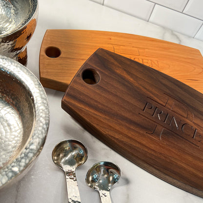 A wooden cheese board with silver spoons and silverware.